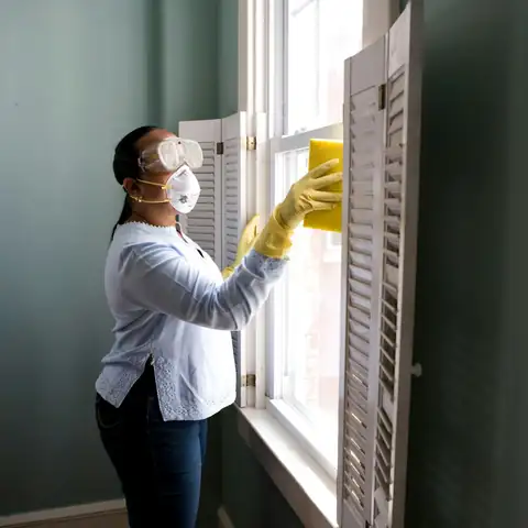 A person in a mask and gloves cleaning window shutters