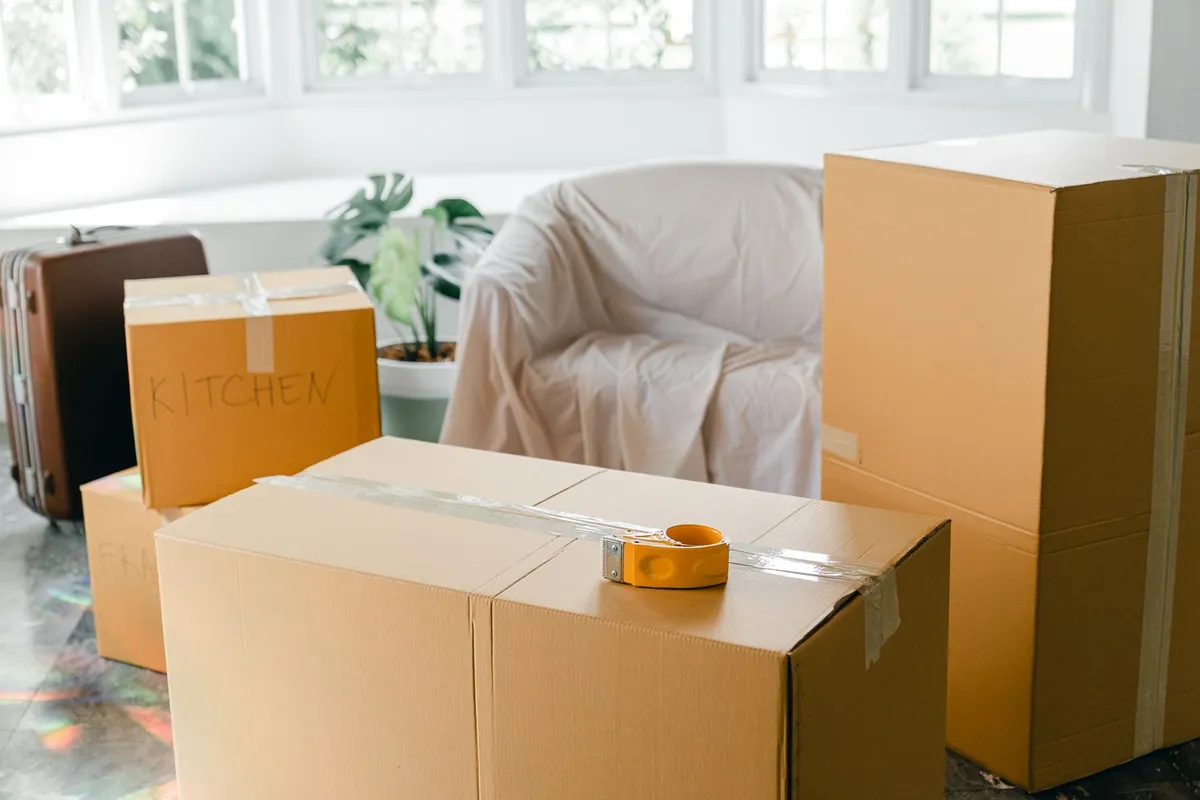 Cardboard boxes and a suitcase filled with belongings in a bright room ready for relocation.