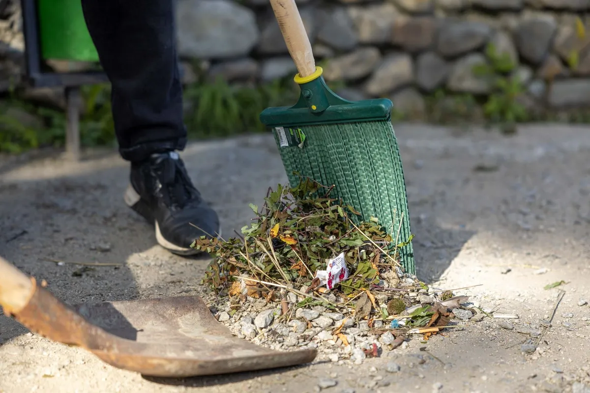 A person raking leaves and debris outdoors, illustrating the need for timely junk removal.